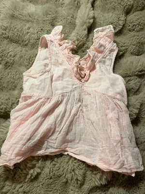 Ljusrosa ärmlös blus med volang - Supersöt ljusrosa blus i tunn bomull med volangdetaljer vid halsen och knytning i nacken. Blusen är ärmlös och har en luftig, flowy passform som känns riktigt somrig och chill.💖