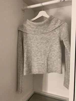 Grå off-shoulder stickad tröja - Mysig ljusgrå ribbstickad tröja som är off-shoulder. Tröjan har långa ärmar och är tillverkad i ett mjukt, fluffigt material som ger en avslappnad och trendig look.
