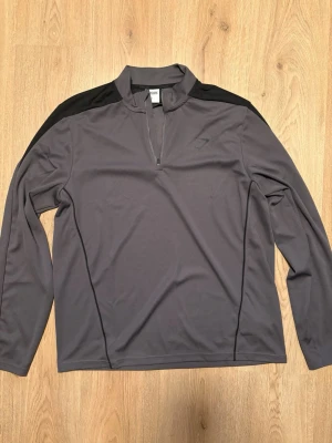 Grå långärmad träningströja Gymshark - Snygg grå långärmad träningströja från Gymshark med svarta axelpartier och halv dragkedja framtill. Tillverkad i ett mjukt och stretchigt funktionsmaterial som andas, perfekt för gymmet eller löprundan. !Knappt använd då den är för stor för mig!