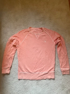 Ljusrosa sweatshirt från Gant - Ljusrosa sweatshirt från Gant med vita kontrastsömmar och rund halsringning. Tröjan har en liten broderad logga på bröstet och är tillverkad i mjuk bomull. Perfekt för en avslappnad och stilren look.