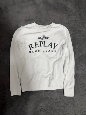 Vit långärmad topp från Replay - Vit långärmad topp från Replay med trycket 'REPLAY BLUE JEANS' i svart på bröstet och en liten logga ovanför texten. Klassisk rund halsringning och mjukt material som känns skönt mot huden. Perfekt för en avslappnad och stilren look.