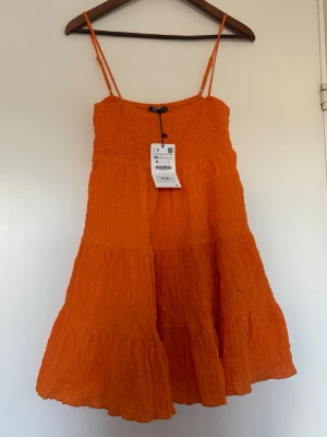 Orange sommarklänning från Zara - Superfin orange klänning från Zara med smala axelband och volangig kjol. I nyskick men har råkat sätta en fläck på den. Kanske går bort i tvättmaskinen