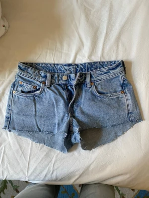 Ljusblå jeansshorts med rå kant - Säljer ett par ljusblå jeansshorts med rå, fransig kant och klassisk femficksdesign. Shortsen har bälteshällor och knappgylf. Perfekta för varma dagar och ger en avslappnad vibe. Använt typ 2 gånger men syns inget. Öppen för prisförslag