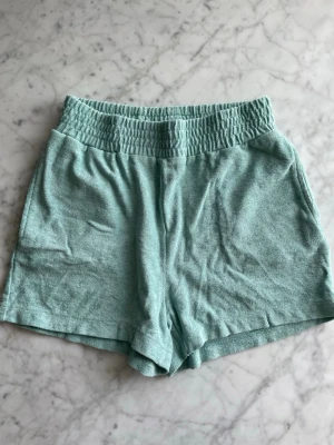  Frottéshorts - Mintgröna/turkosa shorts från Indiska i frotté. Finns två fickor på vardera sida. Är storlek S men stor i storleken enligt mig. Knappt använda.