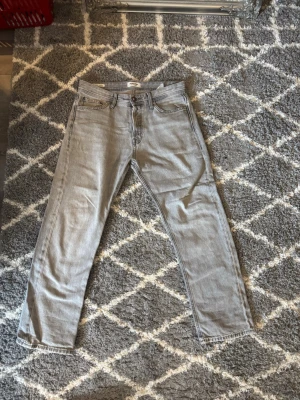 Grå jeans med raka ben - Säljer ett par grå jeans med raka ben och klassisk femficksdesign. Jeansen har knapp och dragkedja framtill samt är tillverkade i ett slitstarkt denim-material. Perfekt för dig som gillar en enkel och stilren look.
