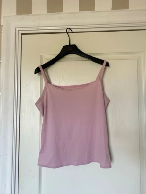 Ljusrosa linne - En enkel och stilren ljusrosa linnetopp med smala axelband. Toppen har rak passform och är perfekt för varma dagar. Materialet känns mjukt och lätt, vilket gör den bekväm att bära. Snygg att matcha med jeans eller kjol. Har tyvärr ingen märkeslapp.