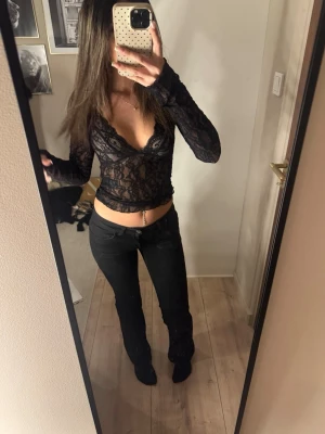 Svart spetsblus med v-ringning - Säljer en svart, transparent spetsblus med djup v-ringning och långa ärmar. Blusen är croppad och har ett feminint, figurnära snitt. Perfekt för dig som gillar trendiga och detaljerade toppar med snygg spets.