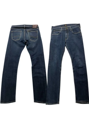 Mörkblå Lee Luke jeans W30 L32 - Snygga mörkblå jeans från Lee, modell Luke. Klassisk femficksdesign med raka ben och kontrastsömmar. Tillverkade i bomull med en liten mängd stretch för extra komfort. Perfekta för en avslappnad och stilren look.