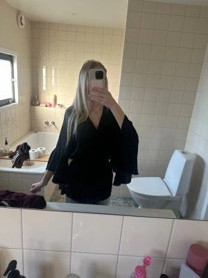 Svart blus med volangärmar och knytskärp - Stilren svart blus med v-ringning, vida volangärmar och knytskärp i midjan. Blusen har en lös passform och är tillverkad i ett mjukt, vävt tyg som ger ett snyggt fall. Perfekt att styla med jeans eller kjol för en trendig look. Skriv om ni har några frågor!💗