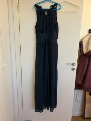 Mörkblå långklänning från Vila - Elegant mörkblå långklänning från Vila med smockad midja och ärmlös design. Klänningen har en stilren, rak passform och ett litet nyckelhål vid halsen. Perfekt för dig som vill ha en klassisk och tidlös look. Endast använd en gång! Kan f mer i pris vid snabb affär!!
