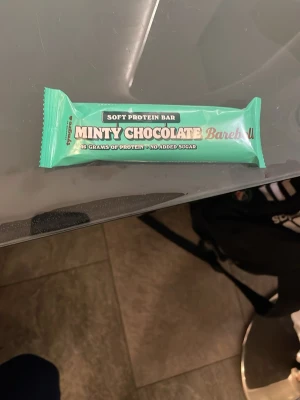 Minty Chocolate proteinbar Barebells - En proteinbar med mintchokladsmak från Barebells. Förpackningen är mintgrön med vit och brun text. Innehåller 16 gram protein och inget tillsatt socker. Perfekt som mellanmål eller efter träning. Den är oöppnad och pris kan diskuteras