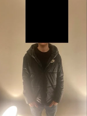 Svart pufferjacka från Nike - Säljer en svart pufferjacka från Nike med huva och dragkedja framtill. Jackan har en klassisk quiltad design och Nike-logga på bröstet. Perfekt för kalla dagar och riktigt skön att bära. Passar dig som vill ha en stilren och sportig look.