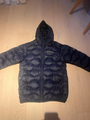 Svart dunjacka från Peak Performance - Snygg svart dunjacka från Peak Performance med huva och hel dragkedja. Jackan har en quiltad design och två sidofickor med dragkedja. Perfekt för kalla vinterdagar och riktigt skön att bära. Liten skada på en av ärmarna. Vid snabbt köp så kan pris diskuteras. 
