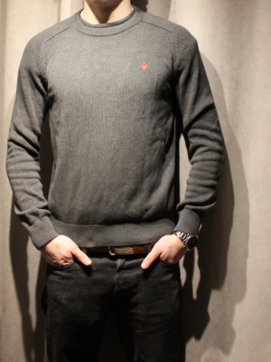 Mörkgrå stickad tröja från Morris - Mörkgrå stickad tröja från Morris med rund halsringning och diskret röd logga broderad på bröstet. Tröjan har långa ärmar och ribbade muddar vid ärmslut och nederkant. Perfekt för lager-på-lager och enkel att matcha. Tröjan är i perfekt skick förutom att den saknar taggen, dock är detta inget som påverkar utseendet alltså har den inga skador eller liknande 🌟 Modellen är 182 och bär vanligtvis S/M. Hör gärna av dig med frågor🤝