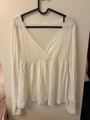 Vit babydoll topp med spets - Söt vit babydoll topp med v-ringning och spetskant längs halsringningen. Vet inte märket! Toppen är i väldigt bra skick!❤️