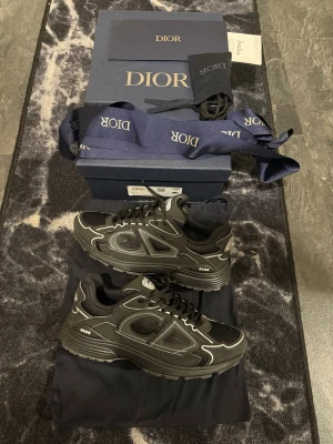Dior B30 - Snygga svarta Dior sneakers (B30) med coola silverdetaljer och meshpaneler. Skorna har chunky sula, tydlig Dior-logga på sidan och en modern design som sticker ut. Perfekta för dig som gillar exklusiva och trendiga sneakers. Size 41.5 men passar 42 alldeles utmärkt! 