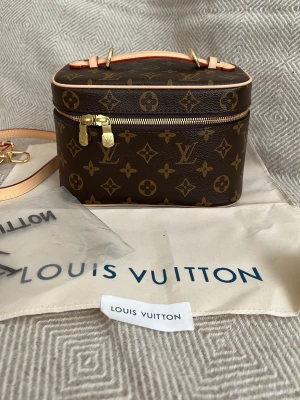 Louis Vuitton Monogram sminkväska  - Snygg handväska/sminkväska/necessär  från Louis Vuitton i klassiskt monogrammönster. Väskan är brun med beige och guldiga detaljer, har en boxig form och dragkedja runt om. Tillverkad i canvas med läderdetaljer och justerbar axelrem. Perfekt för dig som gillar lyxiga accessoarer.
