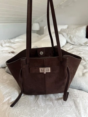 Mörkbrun väska i mocka - Snygg mörkbrun väska i mocka från Gina tricot. Perfekt storlek, inte för stor, men får plats med allt💕💕 Har tre innerfack, varav ett är med dragkedja. Fint skick förutom ett band som var lite slitet, vilket jag lagade själv. Pris kan absolut diskuteras!