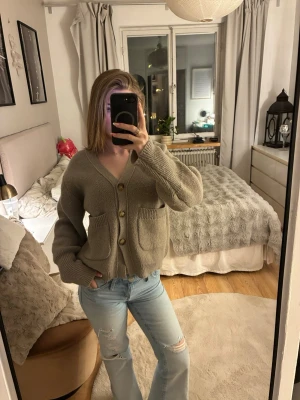 Beige kofta med stora fickor - Säljer en beige, stickad kofta med v-ringning och stora knappar framtill. Koftan har två rejäla fickor och är gjord i ett mjukt material som känns riktigt cozy. Perfekt för lager-på-lager och chill dagar.