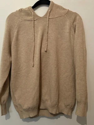 Merinoull hoodie, beige  - Mysig beige merinoull hoodie med huva och dragsnören. Tröjan är otroligt skön att ha på sig och är riktigt schysst. Perfekt för dig som gillar en enkel och stilren look.