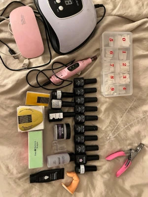 Stort nagelkit med gel och tillbehör - Komplett nagelkit med flera gel-lack i olika färger, UV/LED-lampor, elektrisk nagelfil, tippar i olika storlekar, nagelklippare, buffertar, nagelformar och tillbehör. Acrylen är mindre än halvfull och pudret är vitt och är halvt. Perfekt för kreativa nageldesigner hemma. Färgerna inkluderar rosa, lila, orange, gul och nude. Och sätts i uv lampan när den applicerats 