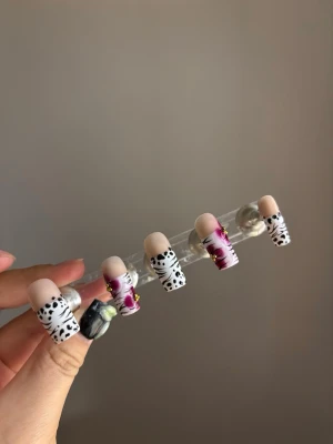 Press-on naglar med dalmatin och lila - Unika press-on naglar i mandelform med dalmatinmönster i svart och vitt samt lila och vita swirl-detaljer. Några naglar har små guldfärgade dekorationer för extra bling. Snygg mix av mönster och färg för dig som vill sticka ut.