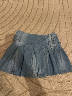 Ljusblå jeanskjol med vidd - Kort ljusblå lågmidjad jeanskjol med utställd passform och fina sömdetaljer upptill. Kjolen har en bred linning och flera veck som ger extra volym. Perfekt för en trendig och avslappnad look. Vintage❤️