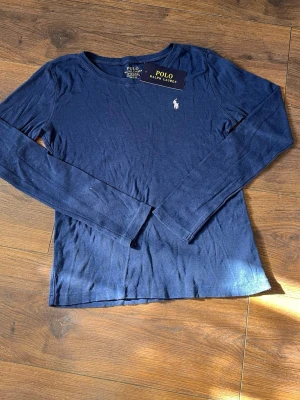 Ralph lauren polo long sleeve i size 150/XS - Mörkblå långärmad tröja från Polo Ralph Lauren med rund halsringning och den klassiska vita logotypen broderad på bröstet. Tröjan är i mjukt och tunt material, perfekt för lager-på-lager och enkel att matcha till olika outfits. Kontakta gärna direkt om ni vill ha fler bilder eller diskutera pris! Skickar samma dag som köp för snabb leverans!