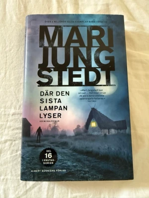 Där den sista lampan lyser - Kriminalroman av Mari Jungstedt, del 16 i Knutas-serien. Omslaget är blått med en mystisk landskapsbild och stora svarta bokstäver. Boken är inbunden och har ett omslag i papper. Perfekt för dig som gillar spännande svensk deckarlitteratur.
