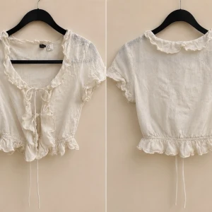 Vit volangblus med knyt i linne - Supersöt vit blus i linne med volangdetaljer längs halsringningen och nederkanten. Knyt framtill och korta ärmar ger en romantisk vibe. Perfekt till jeans eller kjol för en trendig look.