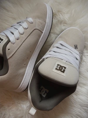 Beige DC shoes - Säljer ett par beige DC sneakers med gröna detaljer och vit sula. Skorna har klassisk låg modell, vit mesh på tungan och stora DC-loggor på sidan. Materialet är mocka och mesh, med vita skosnören och grönt innerfoder.