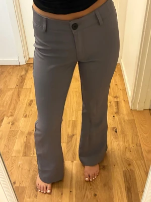 Grå kostymbyxor med bootcut - Snygga grå kostymbyxor med bootcut-modell och hög midja. Byxorna har bälteshällor, knapp och dragkedja framtill samt fejkade bakfickor. Perfekta till en trendig och stilren look.