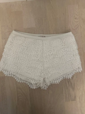 Vita spets-shorts med volangkant - Säljer ett par vita shorts med vacker spets och volangkant.  Perfekta för sommarens alla tillfällen.💕💕