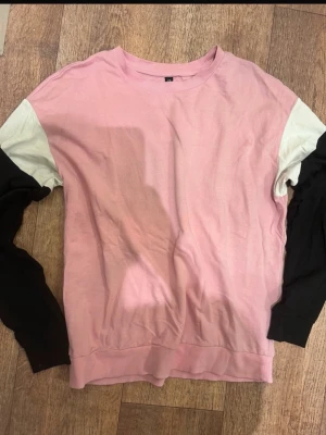 Rosa stickad tröja med kontrastärmar - Säljer en rosa stickad tröja med vita axelpartier och svarta ärmar. Tröjan har rund halsringning och en avslappnad passform. Perfekt för dig som gillar färgblock och en unik stil.