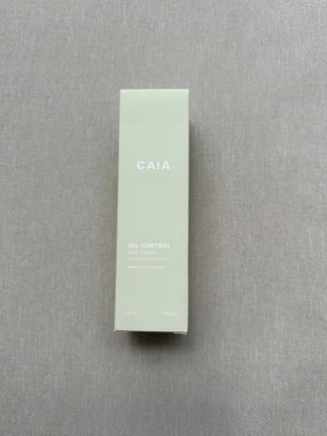 CAIA Oil Control Day Cream - CAIA Oil Control Day Cream i en ljusbeige, rektangulär kartong. Krämen är speciellt framtagen för att kontrollera oljig hud och ge en matt finish. Förpackningen är stilren med vit text och innehåller 50 ml. Perfekt för dig som vill ha en fräsch och balanserad hud.
