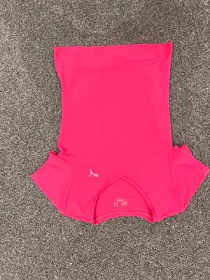 Rosa sportig topp från Puma - Säljer en snygg och sportig rosa topp från Puma med korta ärmar och klassisk logga på bröstet. Perfekt för dig som gillar att träna och vill ha en bekväm och stilren look. Materialet är mjukt och stretchigt polyester.
