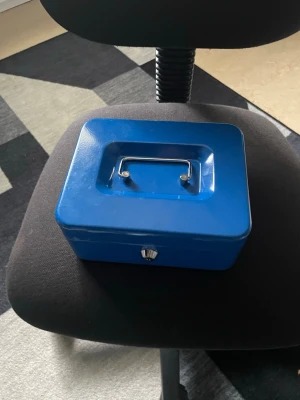 Blå kassalåda med myntfack - Praktisk blå kassalåda i metall med handtag och flera fack för mynt och sedlar. Perfekt för att hålla ordning på pengar eller småsaker. Lådan har ett lås framtill och insats med olika fack för sortering.