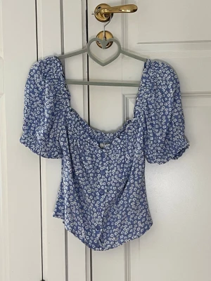 Blommig blå topp med puffärmar - Supersöt blå topp med vita små blommor och puffiga korta ärmar från Nelly. Storlek 38. Bra skick då den enbart är använd ett fåtal gånger. Säljer pga att den tyvärr inte passar mig längre.