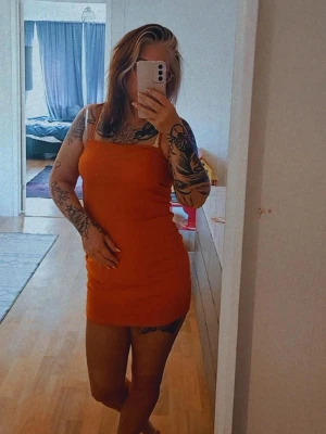 Orange ribbad kort klänning - Säljer en snygg orange ribbad klänning med smala axelband och tight passform. Klänningen är kort och har en enkel, stilren design som passar perfekt till sommaren. Materialet är mjukt och stretchigt för en bekväm känsla. Strl. 38