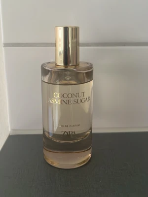 Zara Coconut Jasmine Sugar parfym - Fräsch Eau de Parfum från Zara med doft av kokos, jasmin och socker. Flaskan är cylinderformad i genomskinligt glas med guldfärgad kork och text. Perfekt för dig som gillar söta och blommiga dofter.