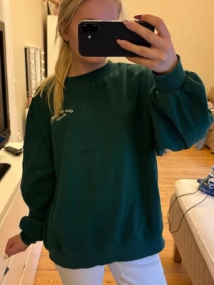 Mörkgrön oversized sweatshirt - En mörkgrön oversized sweatshirt med rund hals och ribbade muddar vid ärmslut och nederkant. Liten vit brodyrdetalj på bröstet där det står "club de sport france". Tillverkad i mjukt sweatshirtmaterial för en chill och avslappnad stil🙌🏻😇 OBS! Har en liten fläck på vänster sidan under texten.