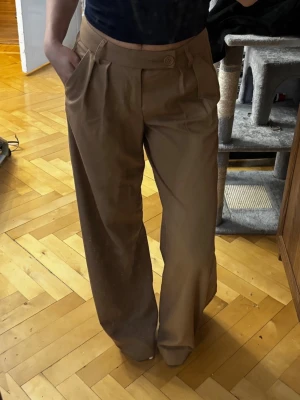 Baggy bruna kostymbyxor med låg midja - Säljer ett par baggy bruna kostymbyxor med låg midja. Perfekta för en clean och stilren look. Materialet känns mjukt och har en lätt glans. Är i mycket bra skicka då de endast använts vid ”special occasions”😂