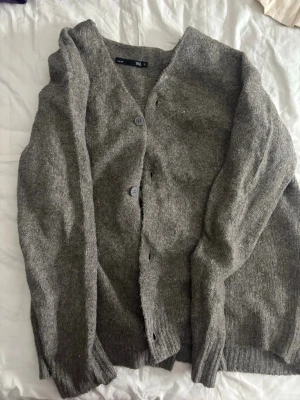 Brun stickad kofta från 157 - Mysig brun stickad kofta från 157 med v-ringning och knäppning framtill. Koftan har långa ärmar och ribbade muddar vid ärmslut och nederkant. Använd 1 gång