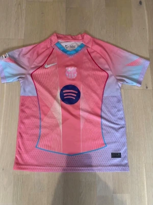 Barça rosa matchtröja Nike - Snygg FC Barcelona matchtröja i rosa och ljusblå toner med tryckta detaljer. Tröjan har korta ärmar, klubbmärke och Nike-logga på bröstet samt Spotify-logga i mitten. På ryggen står det 'LAMINE YAMAL' och nummer 10. Perfekt för fotbollsfans!