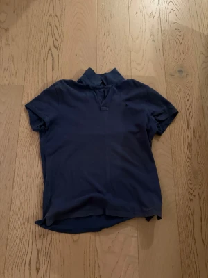 Mörkblå piké med krage - En stilren mörkblå pikétröja med klassisk krage och korta ärmar. Tröjan har en enkel design utan synliga loggor eller mönster och är tillverkad i mjukt bomullsmaterial. Perfekt till jeans eller shorts för en avslappnad look.