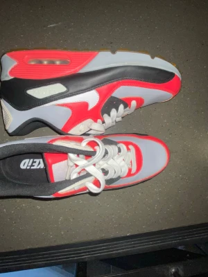 Nike Air Max sneakers röd svart vit - Säljer ett par Nike Air Max sneakers i rött, svart och vitt med klassisk synlig luftbubbla i sulan. Skorna har vita snören, grå detaljer och en gummisula. Perfekt för dig som gillar streetwear och sportig stil.