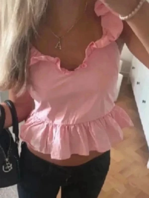 Rosa volang topp med öppen rygg - Supersöt rosa topp med volangdetaljer och öppen rygg med snörning. Toppen är ärmlös och har en croppad passform som ger en fräsch och somrig vibe. Perfekt för dig som vill sticka ut lite extra med en feminin och trendig look.