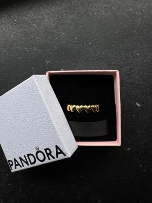 Pandora ring i guld med hjärtan - Superfin ring från Pandora i guldton med små hjärtan runt hela ringen. Kommer i original ask. Perfekt för dig som gillar söta och stilrena smycken med en romantisk touch. Storlek 17,5 nypris 650kr