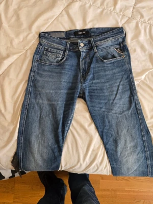Blå slim fit jeans från Replay w29 L30 - Snygga blå slim fit jeans från Replay med klassisk femficksmodell och diskreta slitningar. Jeansen har normal midja, dragkedjegylf och är tillverkade i ett mjukt denimtyg som ger en bekväm känsla. Perfekta för en avslappnad och trendig look.