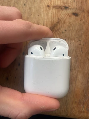 Apple AirPods med laddningsetui - Säljer ett par vita Apple AirPods med tillhörande laddningsetui. De är trådlösa in-ear hörlurar i klassisk Apple-design med slimmad form och laddas via Lightning-port. Perfekta för musik, poddar och samtal på språng. Väntra air podden är knappt fungerande.